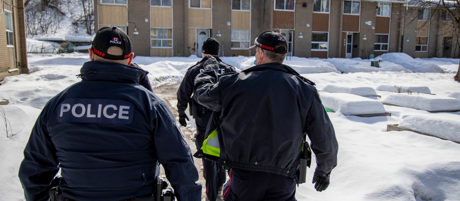 A group of Ottawa Police Service members walking through a residential complex in the winter.